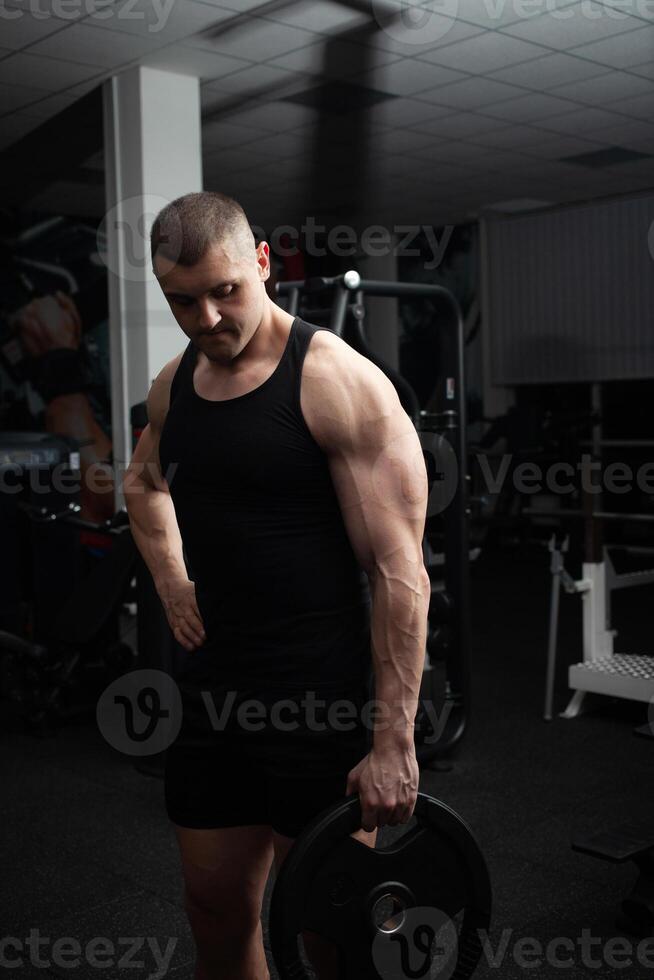 Portrait of a handsome man in gym. Coach, athlete, bodybuilder, muscular sexy body, darkness. photo