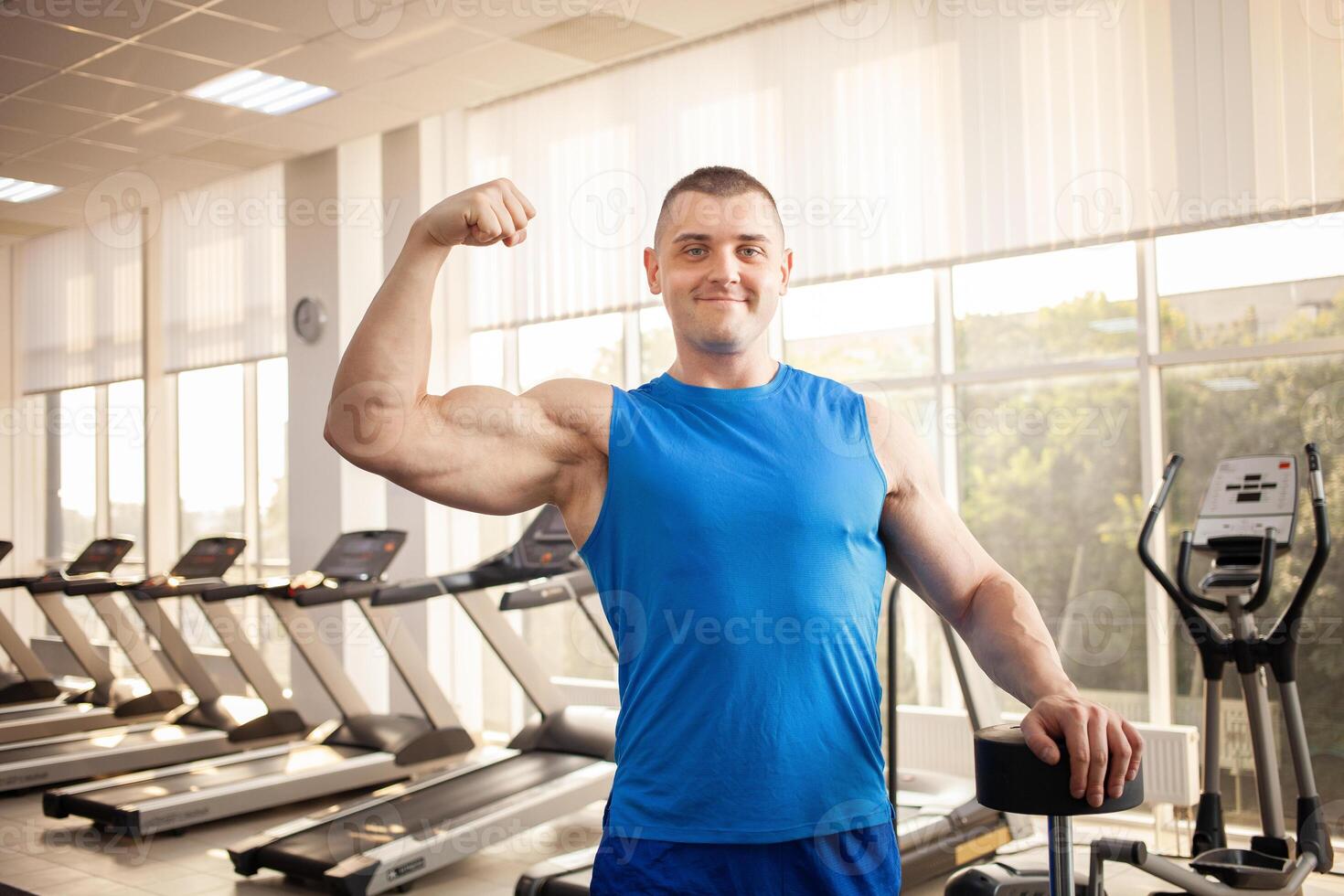 A young handsome coach with a muscular body poses in gym. Bodybuilder, sports physical therapy, weight loss. Sport is a cool, healthy active lifestyle. Indoor concept. portrait photo