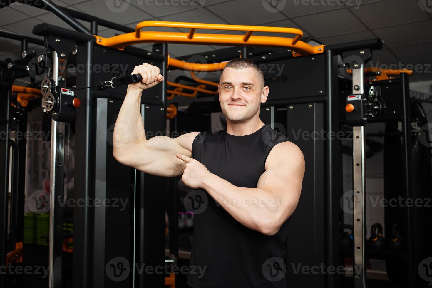 young handsome coach in a black uniform against background of a simulator in gym. Muscular athletic body of a bodybuilder, coaching, individual sports and weight loss Portrait. muscles on the arm photo