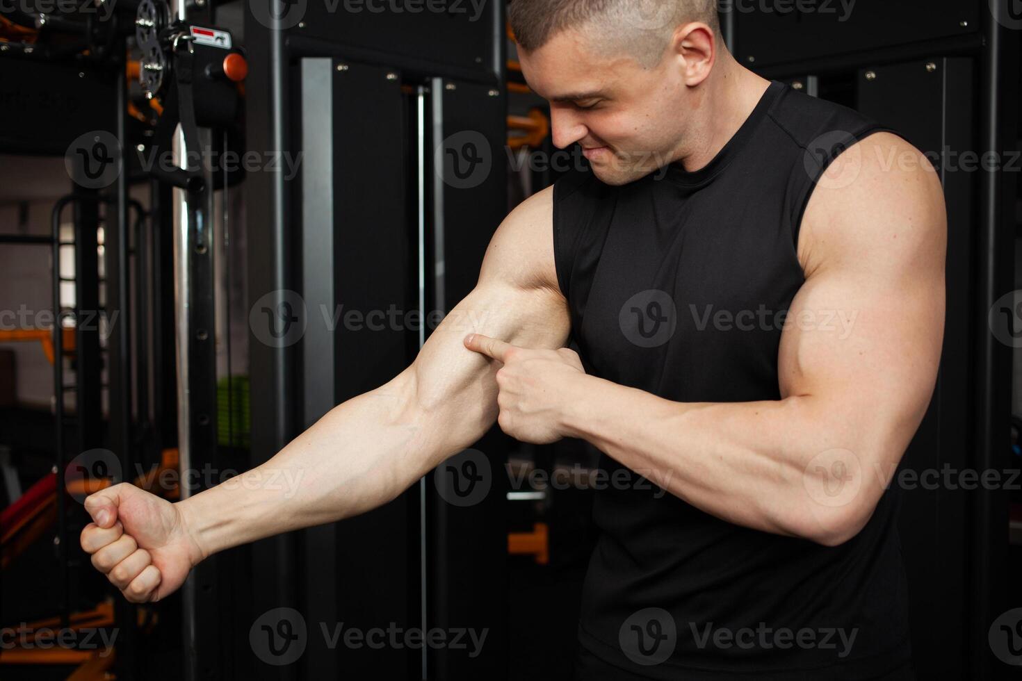 young handsome coach in a black uniform against background of a simulator in gym. Muscular athletic body of a bodybuilder, coaching, individual sports and weight loss courses. Portrait. anatomy photo