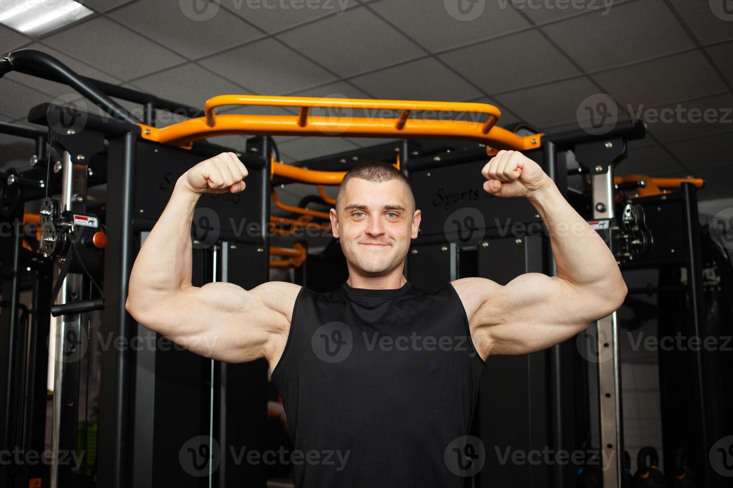 young handsome coach in a black uniform against background of a simulator in gym. Muscular athletic body of a bodybuilder, coaching, individual sports and weight loss courses. Portrait. strong photo