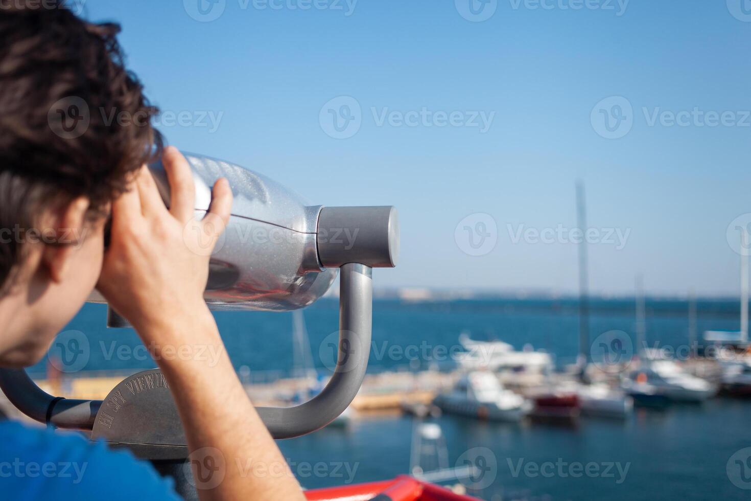 man looks through stationary binoculars. Binoscope on observation deck near sea. seaport in Odessa. Expensive yachts on the pier. Commercial machine, vending business. close up photo