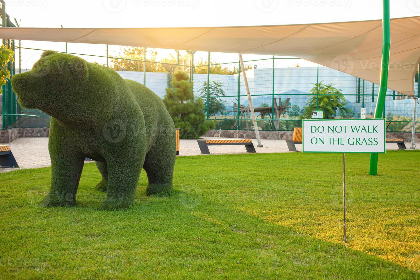 Beautiful bear sculpture of grass, artificial animal, garden decoration. Sign Don't walk on the grass. Sunset photo