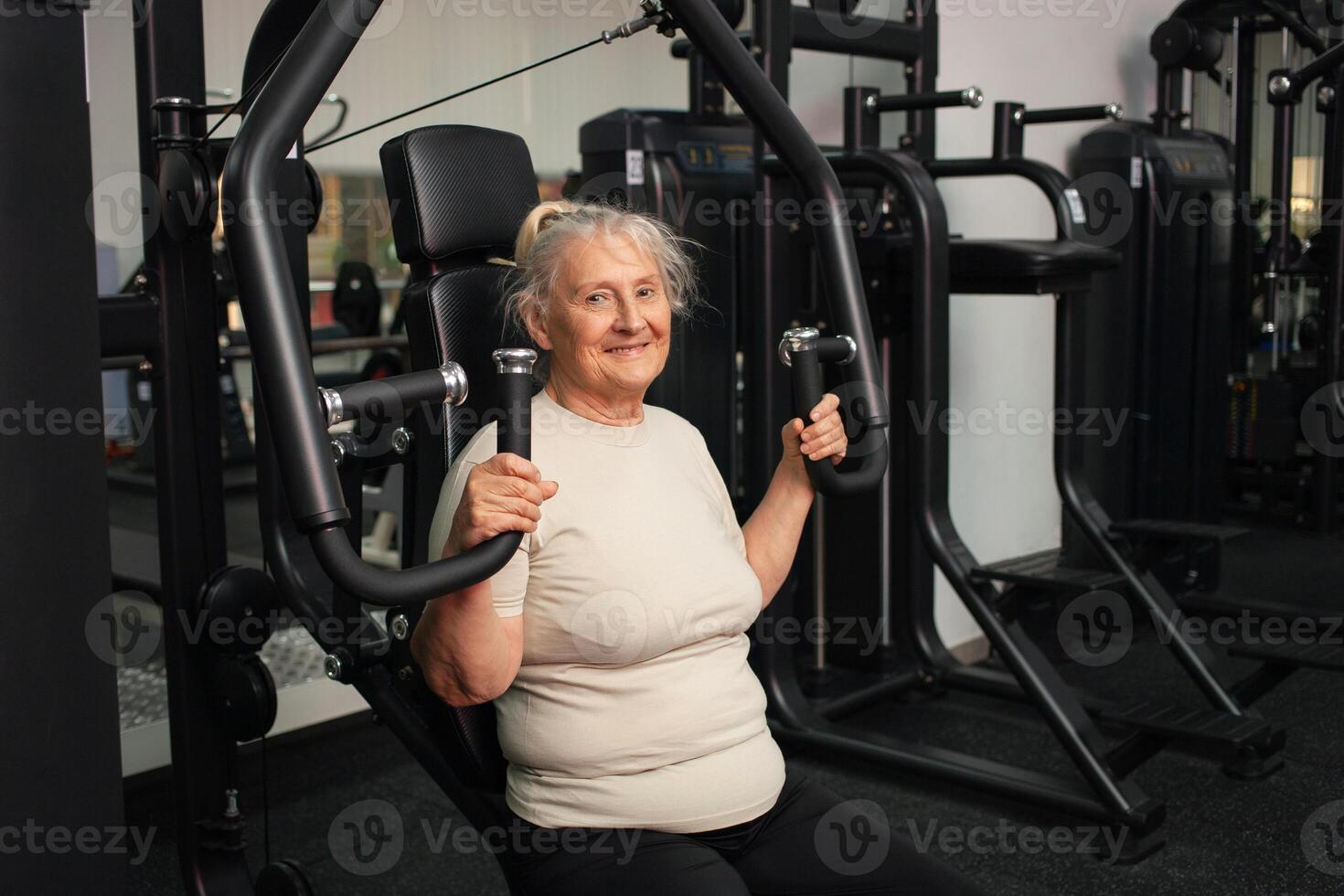 Portrait of a happy pensioner in gym. An old woman goes in for sports on simulators, rejoices, smiles, enjoys, an active healthy lifestyle. photo