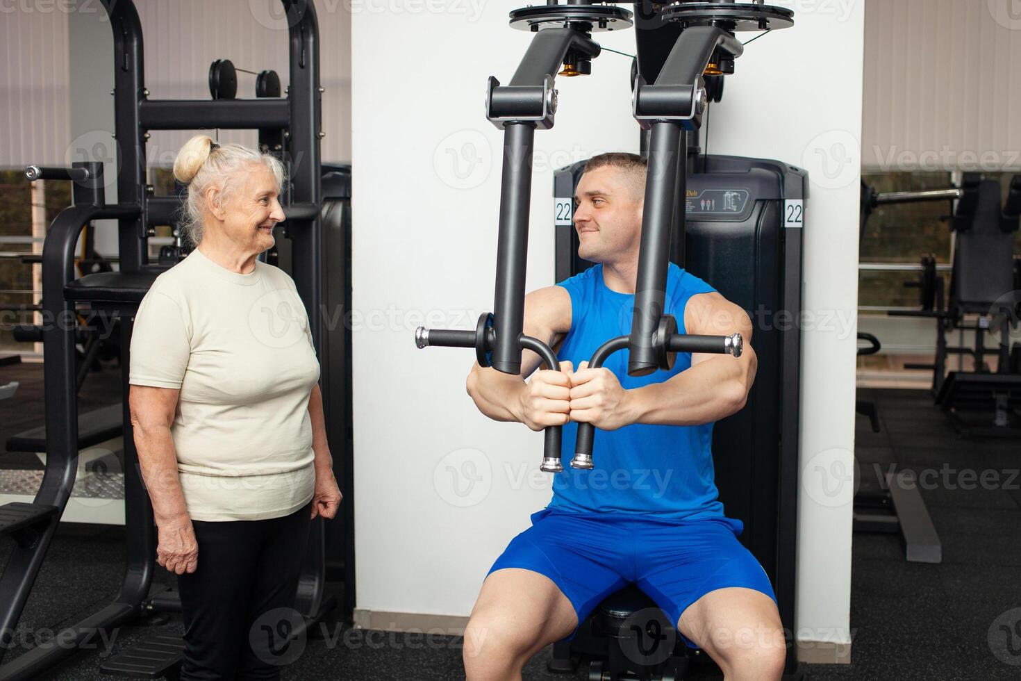 handsome young coach man shows senior woman how to properly perform exercises on the simulator in the gym. Happy people smile, enjoy, happy. Active sports healthy lifestyle indoor. portrait photo