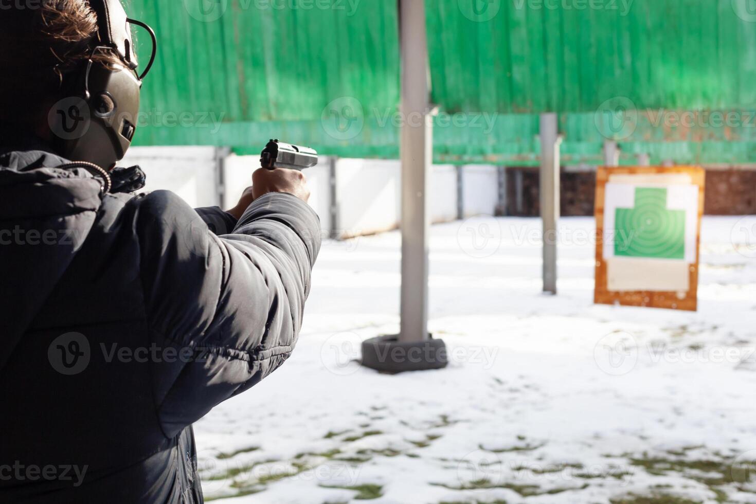 A man with headphones is aiming at the target. A man in a dash fires a gun. Sports entertainment Out the door. photo