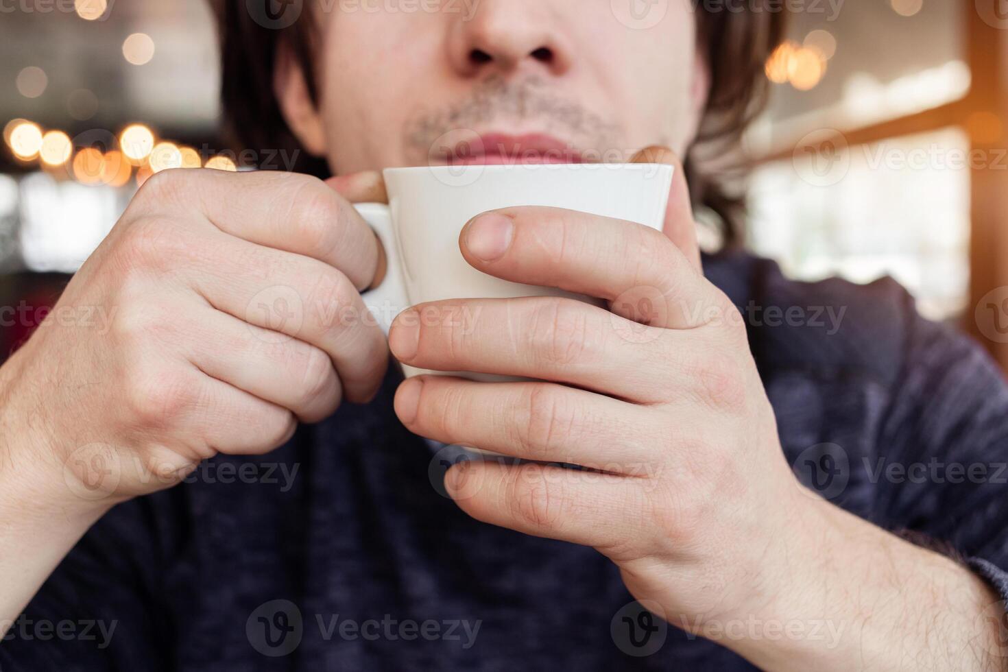 A man drinks coffee in a cafe, a restaurant. interior, natural sunlight, blurred background, sideways. Snack, breakfast. Lunch break. photo