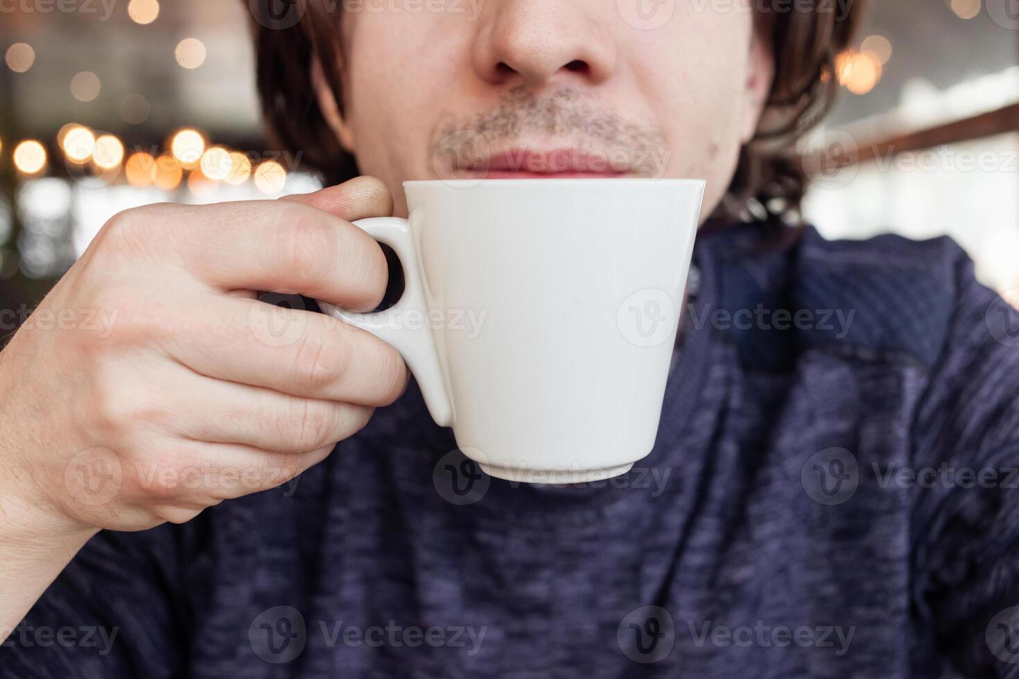 A man drinks coffee in a cafe, a restaurant. interior, natural sunlight, blurred background, sideways. Snack, breakfast. Lunch break. photo