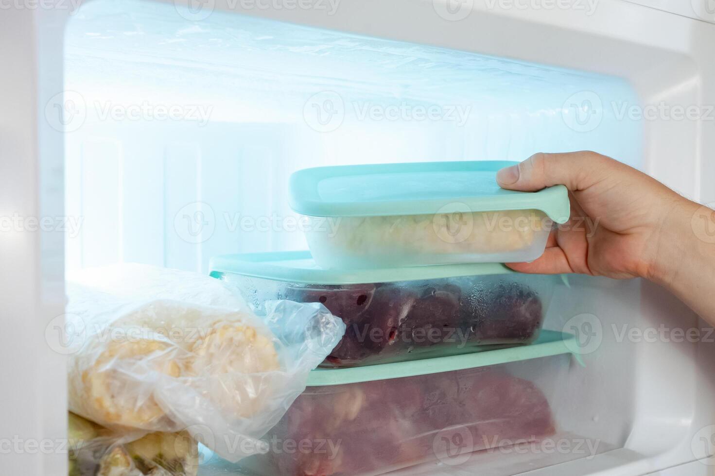 A man pulls frozen vegetables out of the freezer. A man takes corn from the fridge. Plastic containers with frozen meat, vegetables and fruits. photo