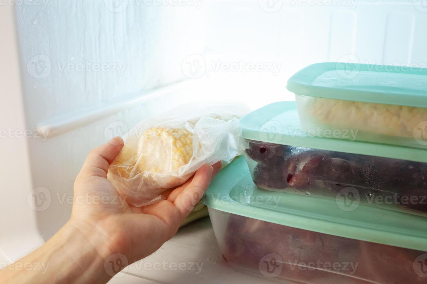 A man pulls frozen vegetables out of the freezer. A man takes corn from the fridge. Plastic containers with frozen meat, vegetables and fruits. photo
