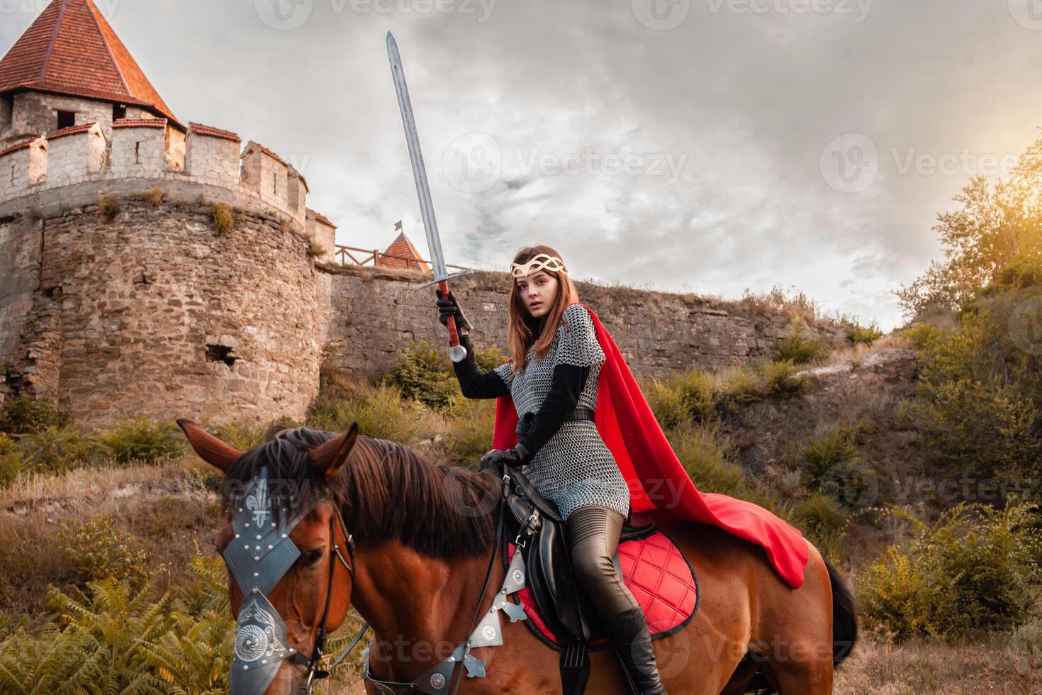 Beautiful Princess with Red Cape and with a sword Riding a Horse against the backdrop of a tower and a stone wall photo