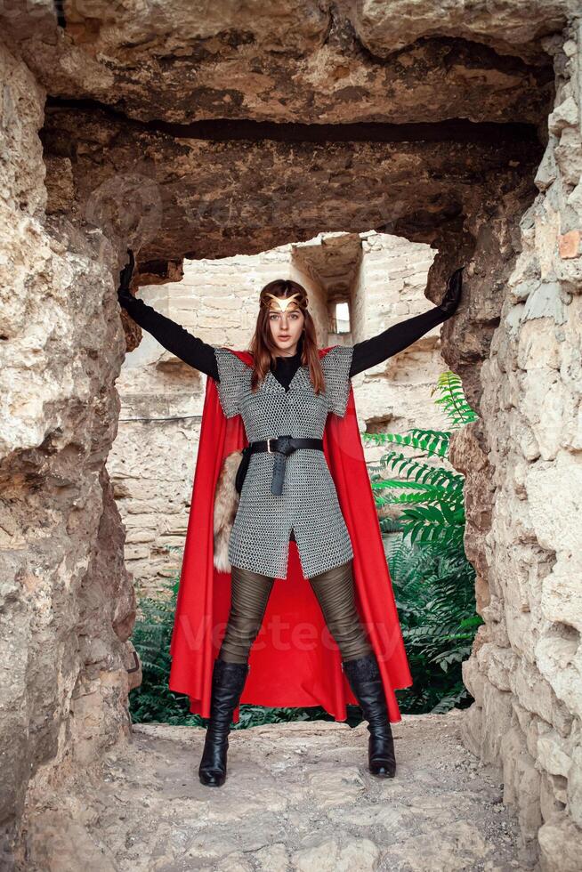 Beautiful Princess with Red Cape and a golden tiara against the stone wall of the tower. photo