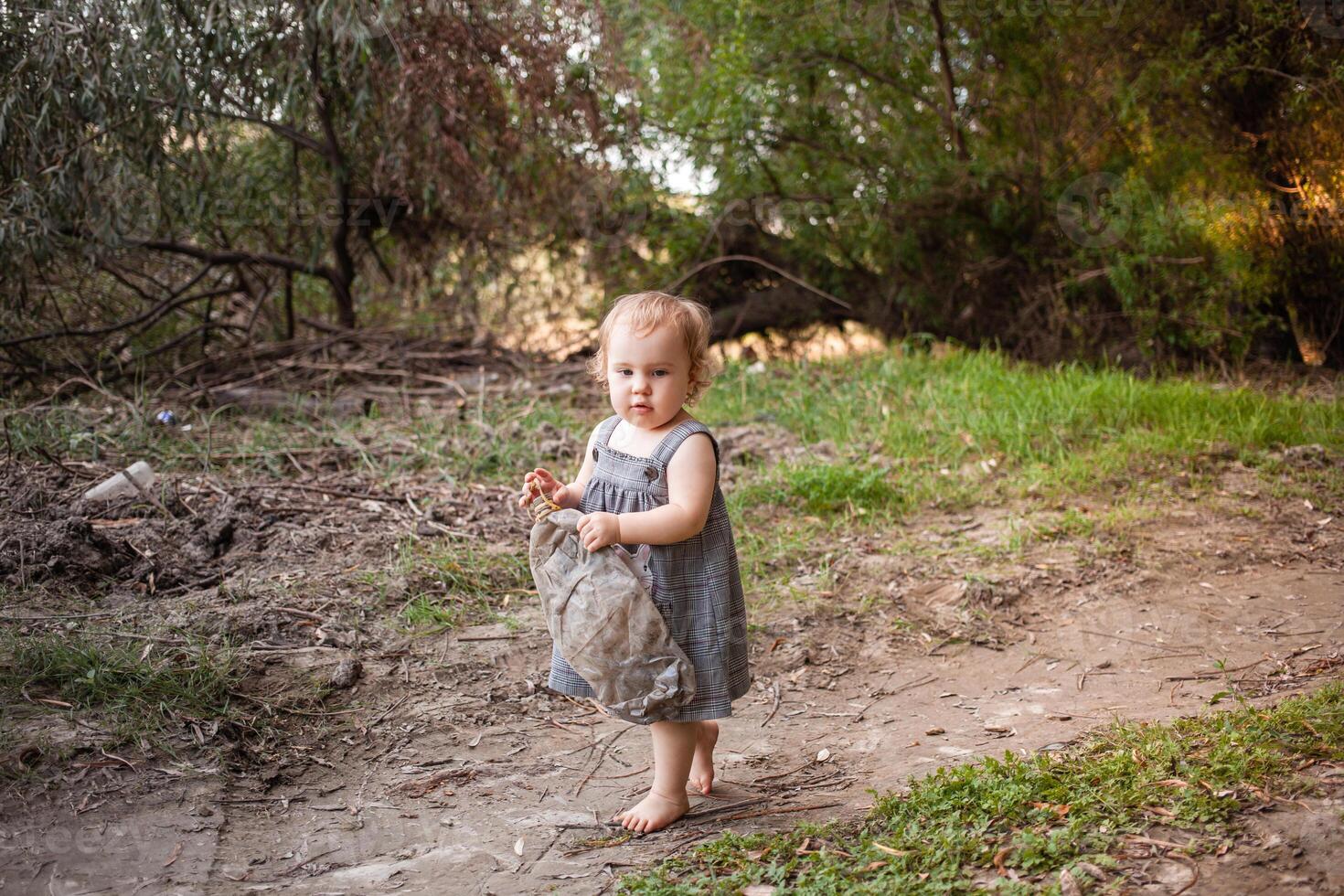 un niño recoge basura en el bosque, un pequeño niña lleva un el plastico botella en contra un antecedentes de hermosa arboles el niño encontró un basura lata en el bosque. proteger el ambiente foto