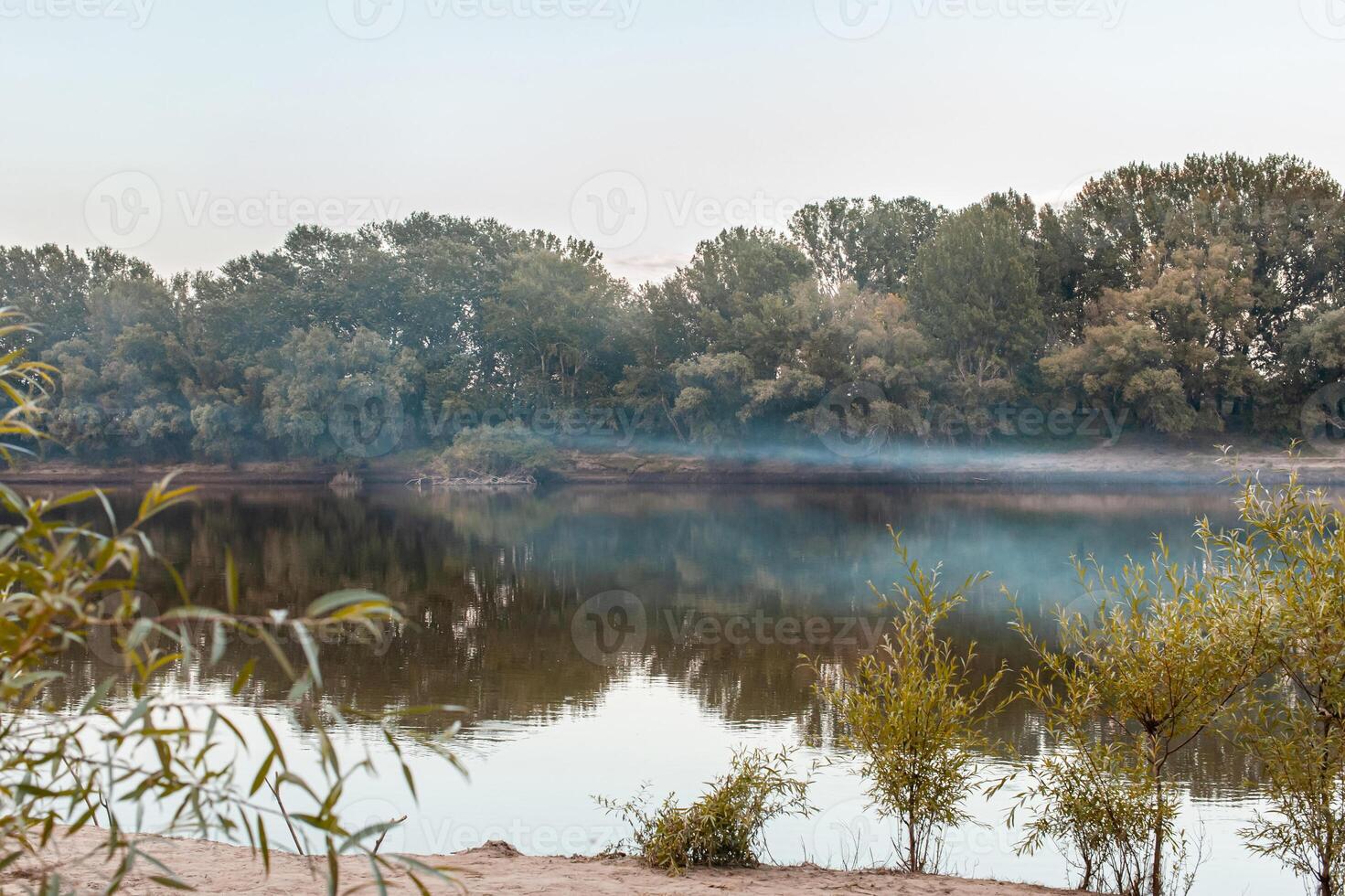 Fog over the river. The river Dniester, blue smoke, smog from the fires. Yellow-green trees on the bank. photo