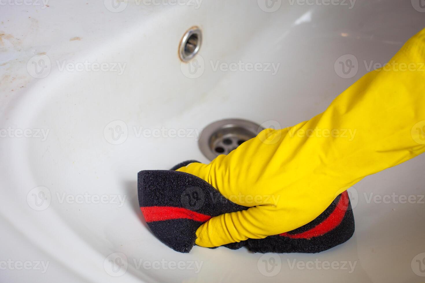 Maid with rubber glove cleaning tap and sink. photo