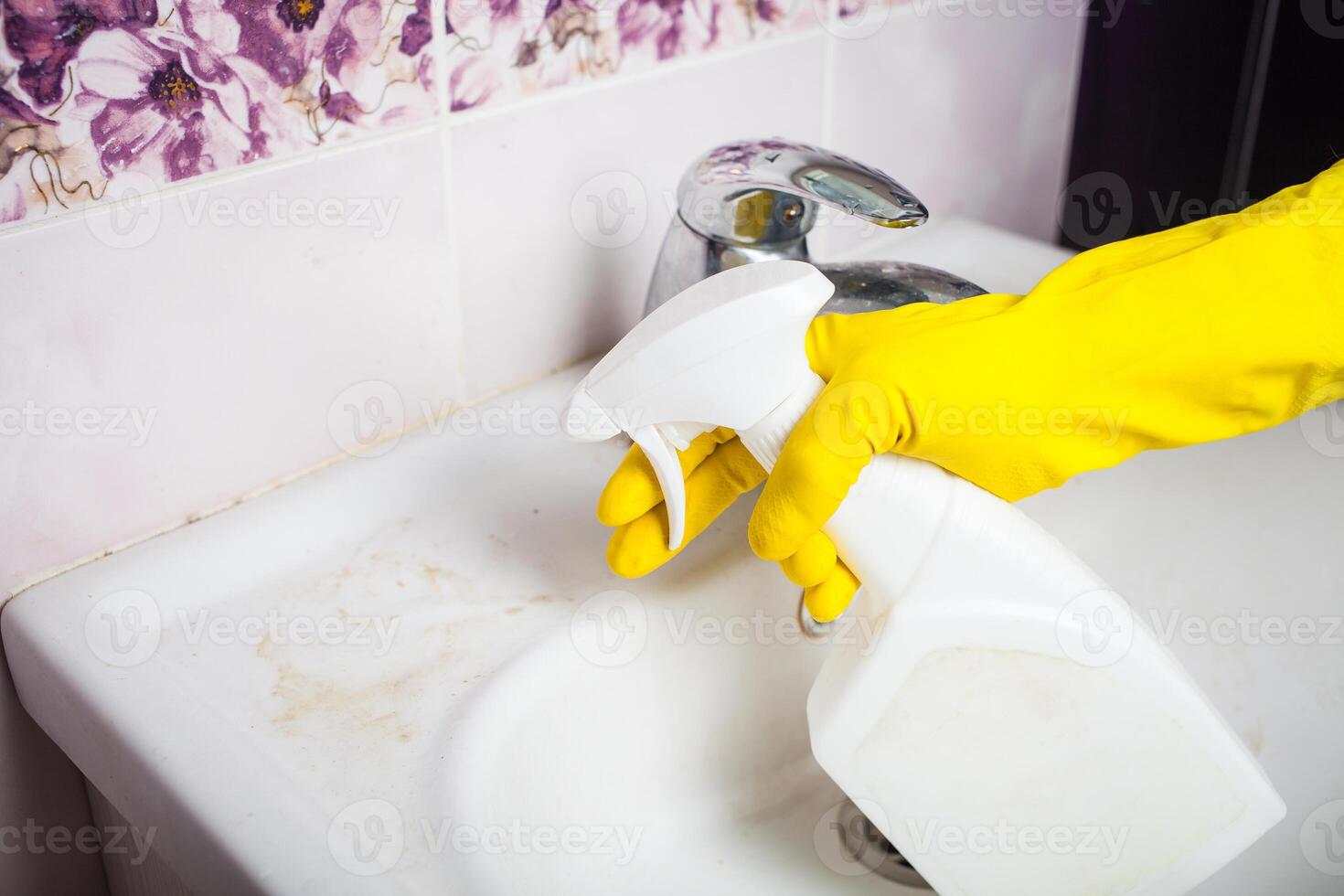 Maid with rubber glove cleaning tap and sink. photo