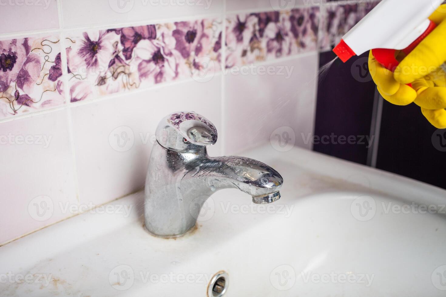 Maid with rubber glove cleaning tap and sink. photo