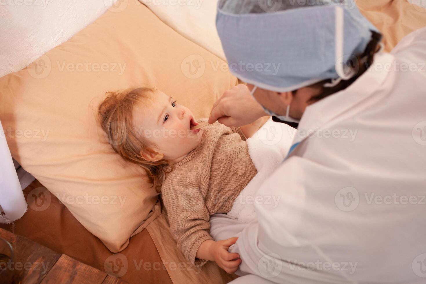 The doctor checks the throat of a little girl at home. Sick baby, home quarantine, coronavirus photo