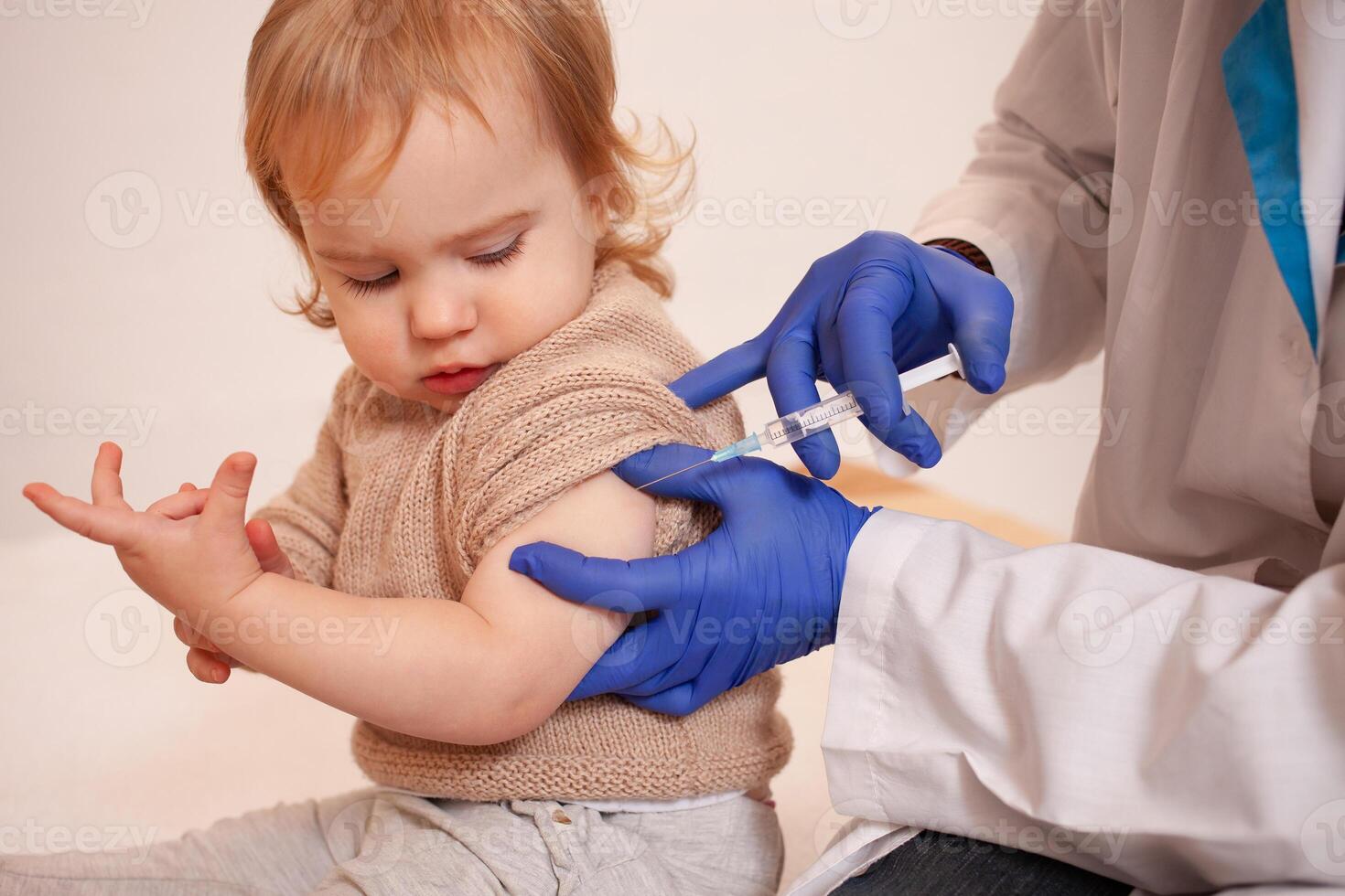 The doctor vaccinates the child against coronavirus. The child is crying and afraid. A man in a robe, hat, mask and gloves makes an injection to the child. Home quarantine photo
