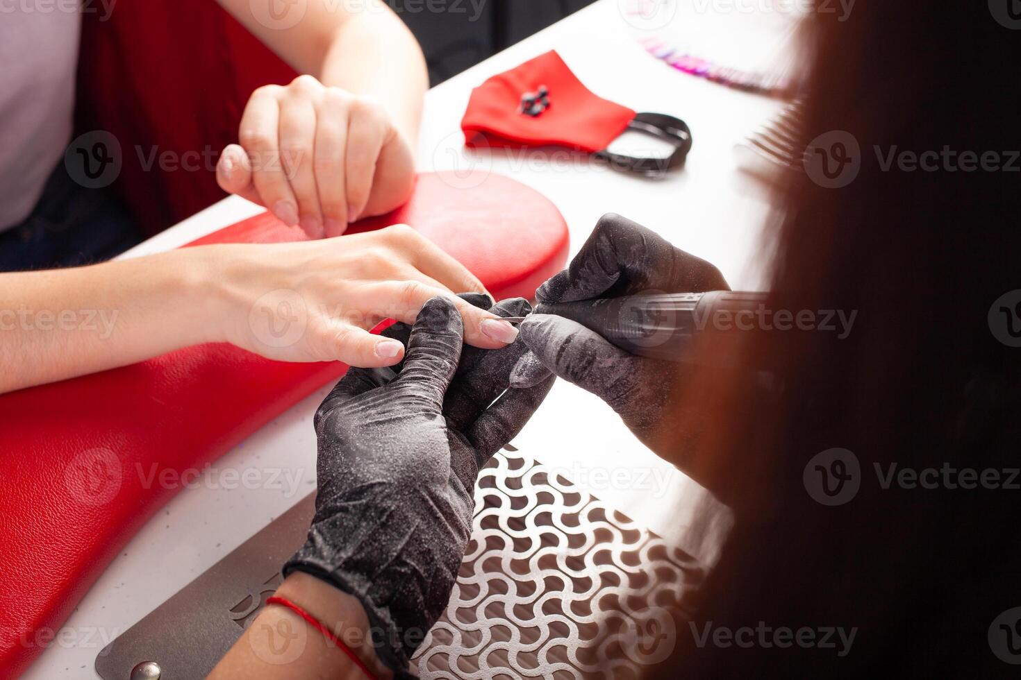 The manicurist holds hands of the client in beauty salon on desktop for manicure with nail polishes, napkins, creams and lighting instruments photo