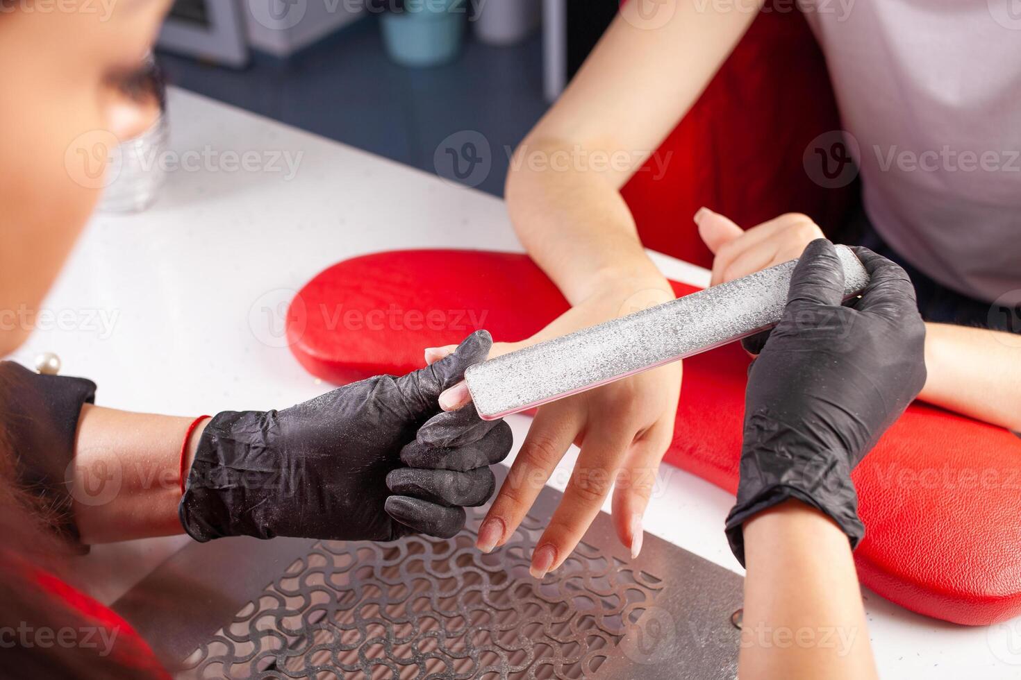 The manicurist holds hands of the client in beauty salon on desktop for manicure with nail polishes, napkins, creams and lighting instruments photo