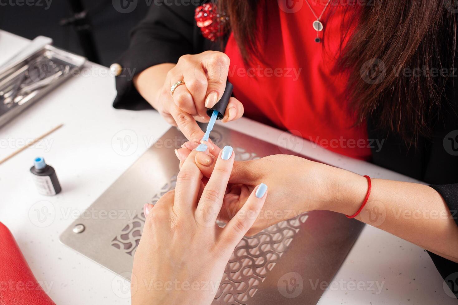 The manicurist holds hands of the client in beauty salon on desktop for manicure with nail polishes, napkins, creams and lighting instruments photo