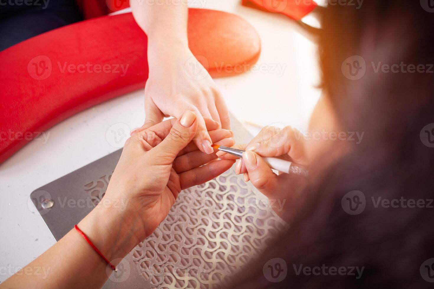 The manicurist holds hands of the client in beauty salon on desktop for manicure with nail polishes, napkins, creams and lighting instruments photo