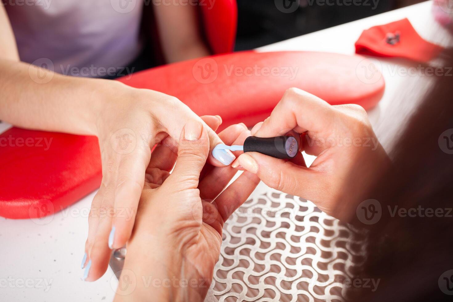 The manicurist holds hands of the client in beauty salon on desktop for manicure with nail polishes, napkins, creams and lighting instruments photo