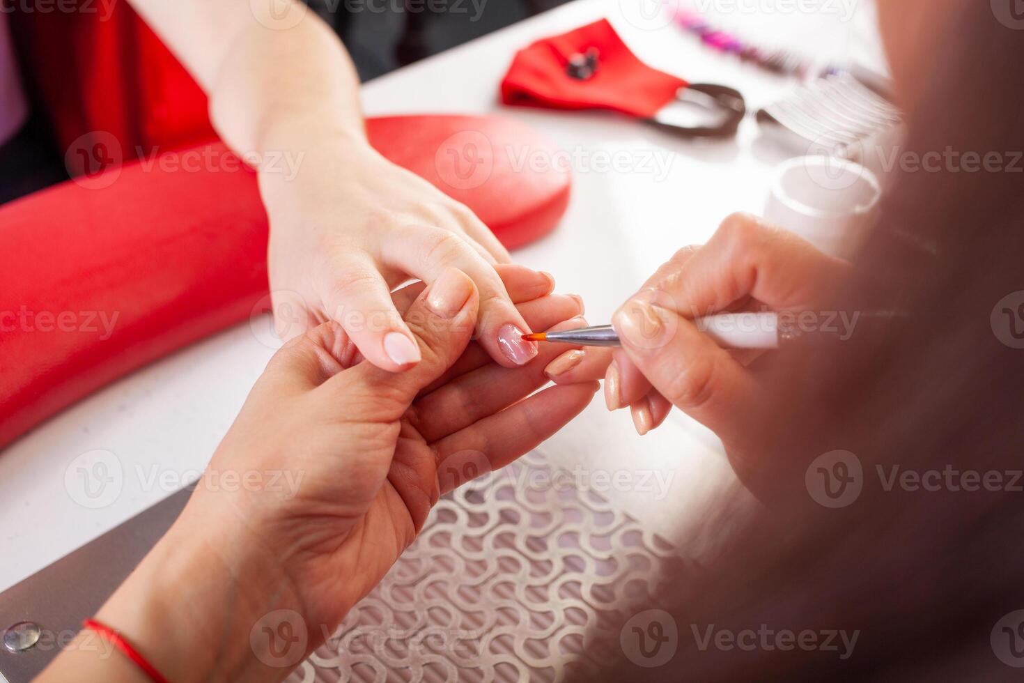 The manicurist holds hands of the client in beauty salon on desktop for manicure with nail polishes, napkins, creams and lighting instruments photo