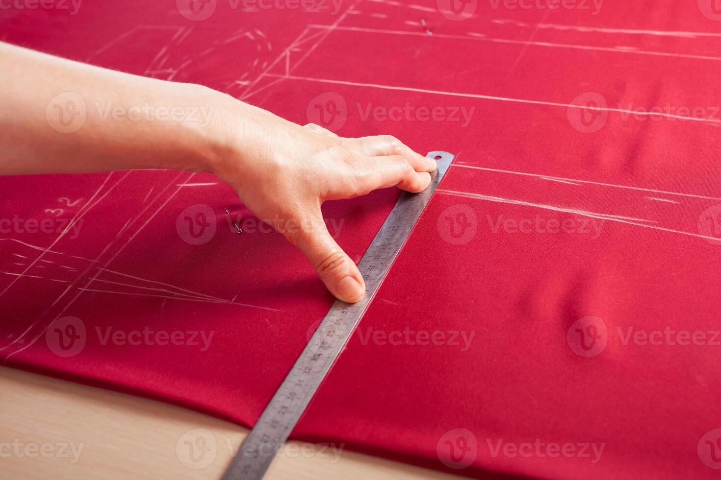 Seamstress at work. Dressmaker making clothes in modern studio. Tailor holding pencil and marking fabric. Woman standing at table with cut textile, sewing machine, thread, pins, needles, tape, cutouts photo