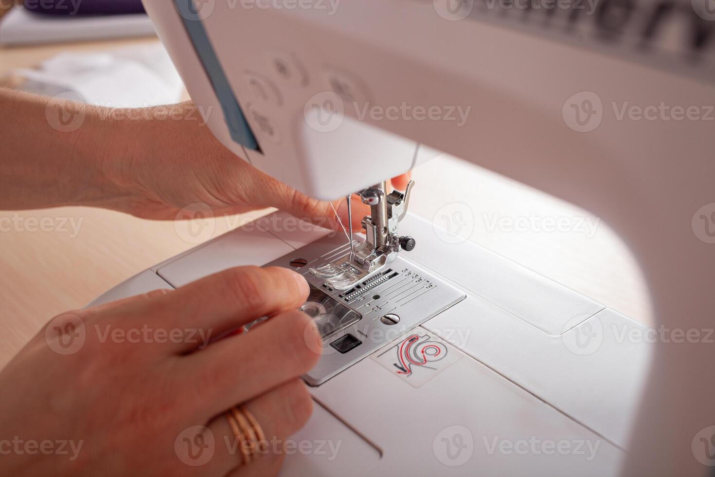 Seamstress at work. Dressmaker making clothes in modern studio. Tailor holding pencil and marking fabric. Woman standing at table with cut textile, sewing machine, thread, pins, needles, tape, cutouts photo