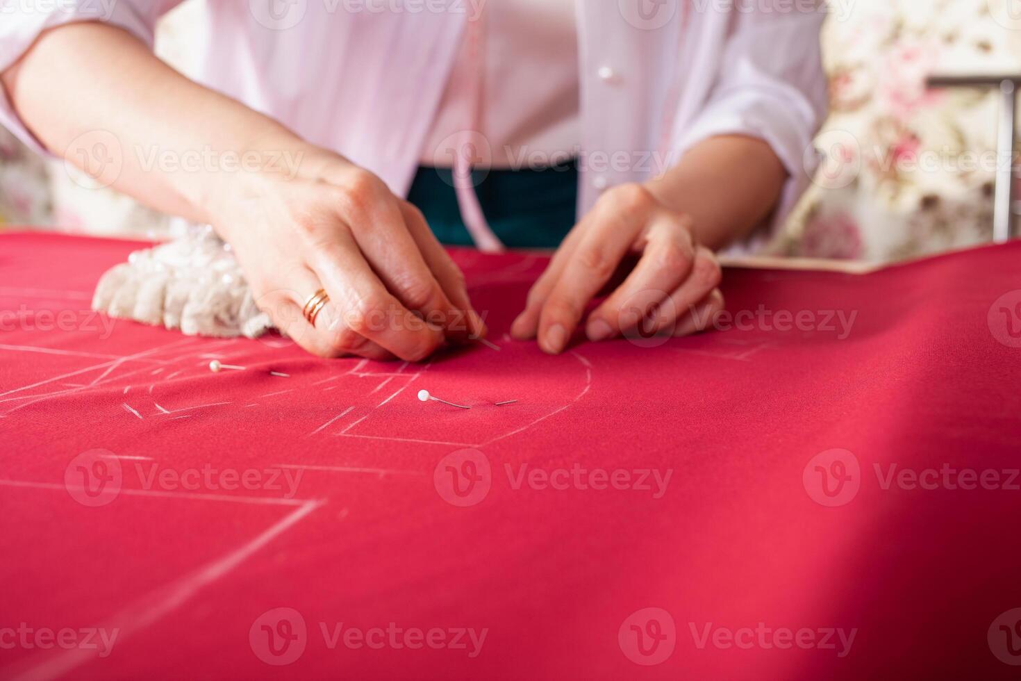 Seamstress at work. Dressmaker making clothes in modern studio. Tailor holding pencil and marking fabric. Woman standing at table with cut textile, sewing machine, thread, pins, needles, tape, cutouts photo