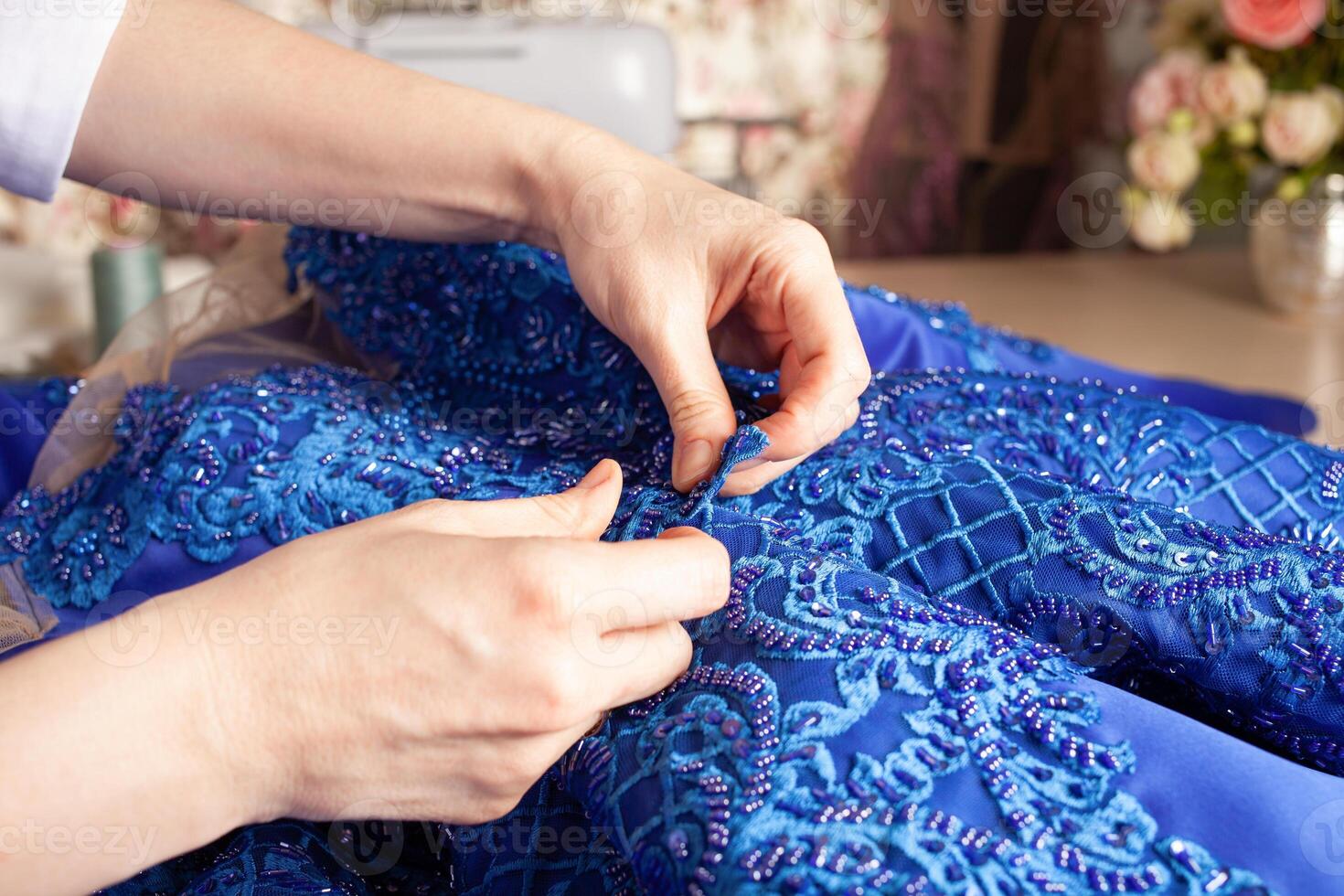 Seamstress at work. Dressmaker making clothes in modern studio. Tailor holding pencil and marking fabric. Woman standing at table with cut textile, sewing machine, thread, pins, needles, tape, cutouts photo