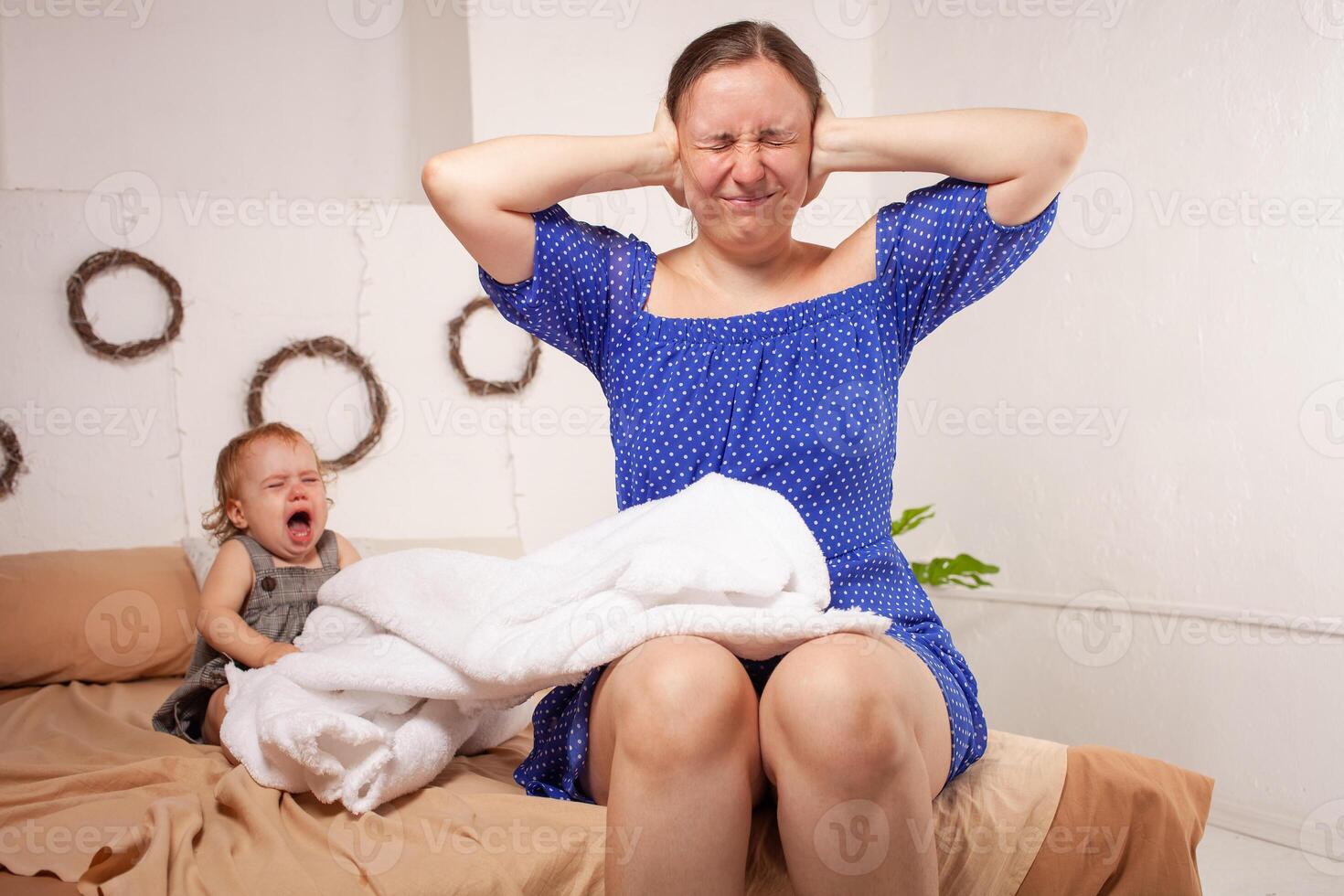 Mom is tired of the baby, wants to rest and sleep. The child screams, hysterical. The woman is tired of the child's cry, she does not want to hear. A one-year-old girl yells from a toothache. photo