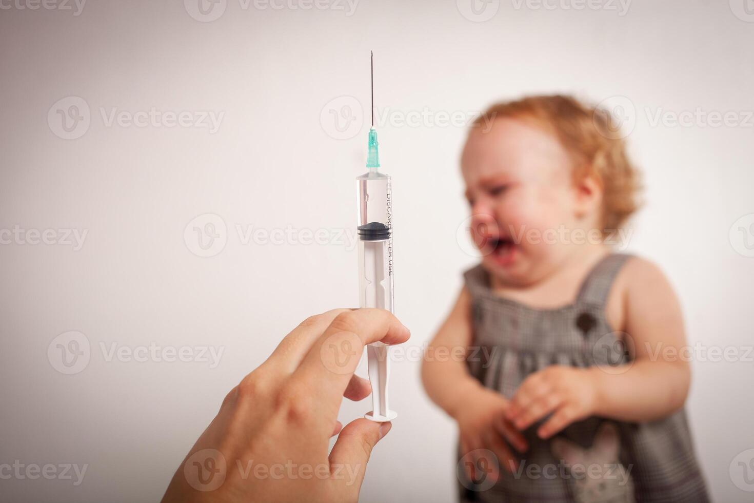 The child is afraid of a syringe, the girl yells and does not want to give an injection. Children's fear of medical procedures. A girl looks at the syringe and screams. Vakination photo