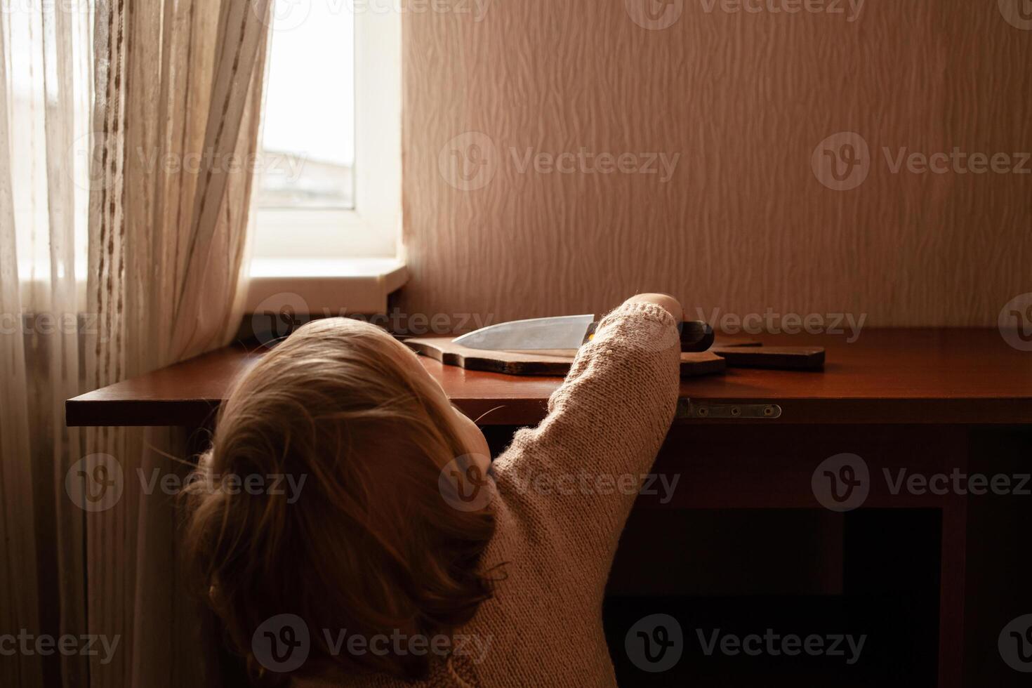 el niño tira un cuchillo desde el mesa. el niño lata cortar, para niños hogar peligros un pequeño un año de edad niña con un cuchillo. foto