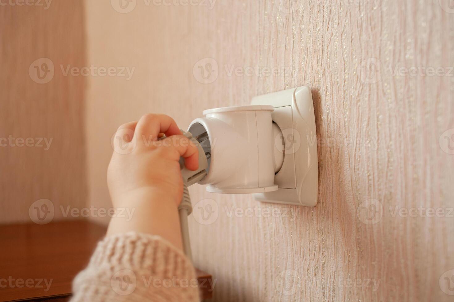 The child plays with an outlet, pulls his hands to it, sticks his fingers. The child is in danger at home. Baby fingers in the socket. photo