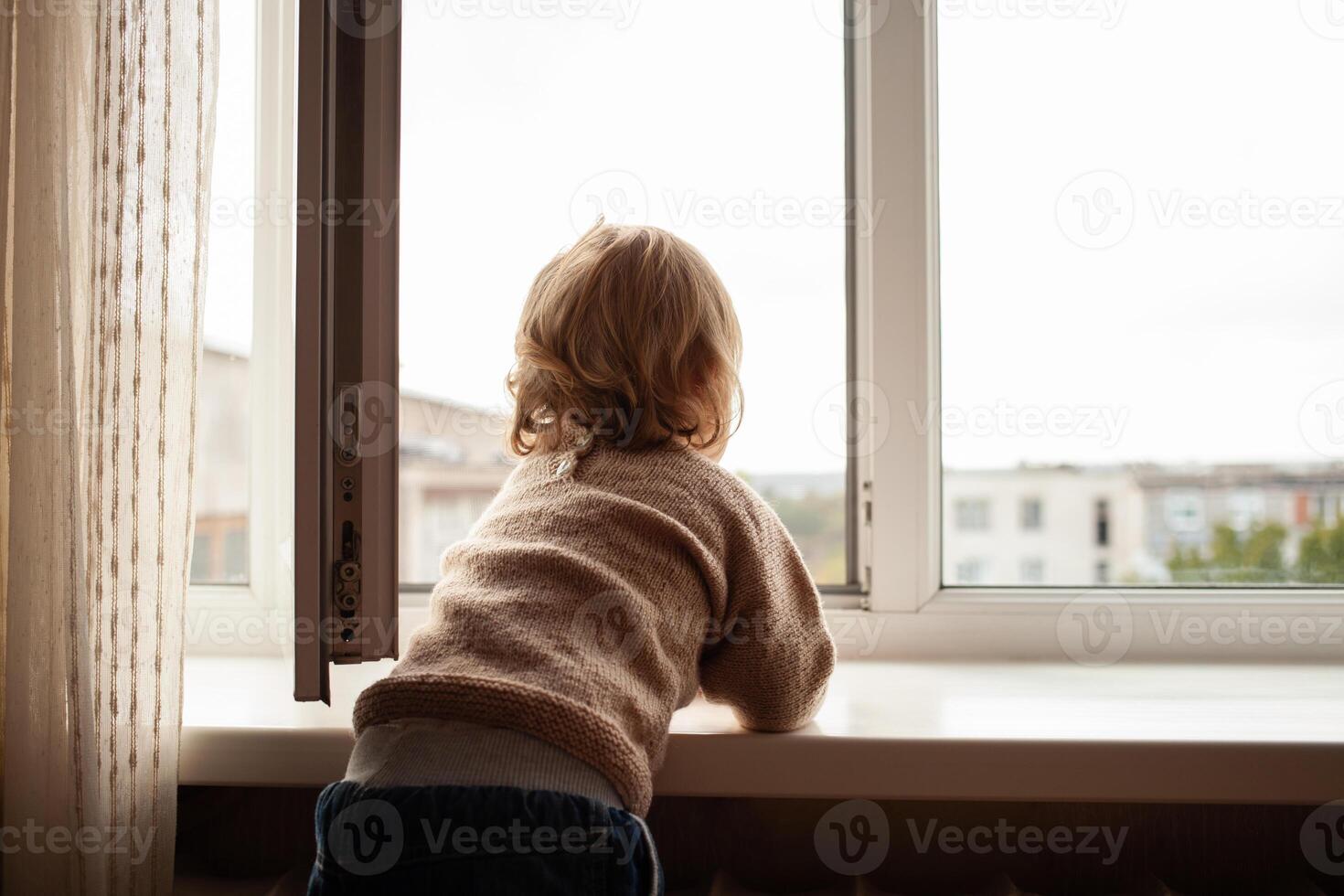The child climbs to the window, the girl on the window sill rests on the net, the danger of falling. The child is alone at home, can fall out of the window. photo
