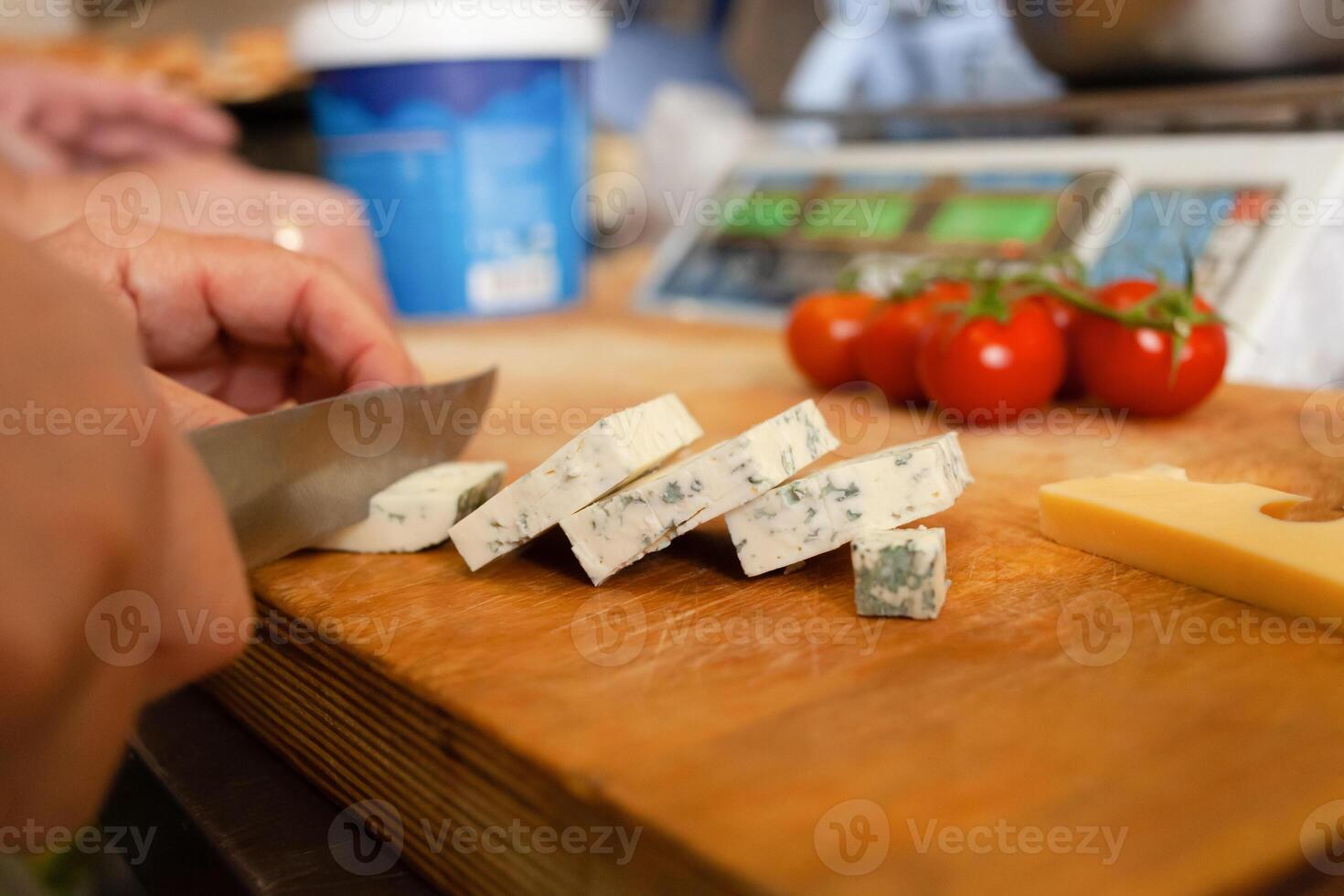 A woman cuts cheese with mold on a wooden board. In the background are scales photo