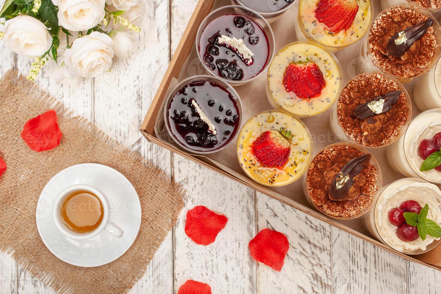 Sweet dessert in glass with biscuit,berry fruit and whipped cream. A cup of tea, flowers, cakes in a box. Delivery of food to the house for parties or a dinner photo