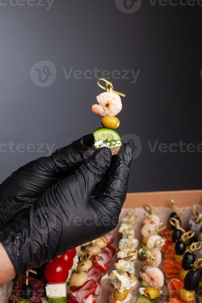 Canape, hands in black gloves hold a beautiful canape on a cap. Catering, snacking, food. Studio photo. photo