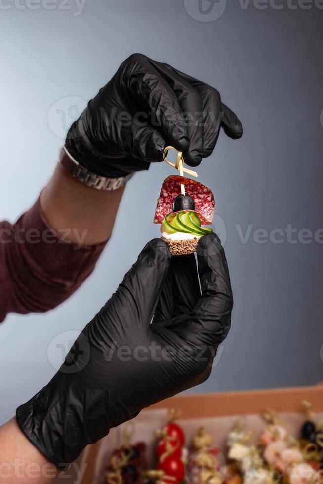 Canape, hands in black gloves hold a beautiful canape on a cap. Catering, snacking, food. Studio photo. photo