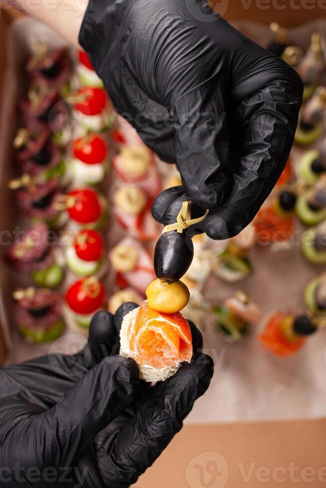 Canape, hands in black gloves hold a beautiful canape on a cap. Catering, snacking, food. Studio photo. photo