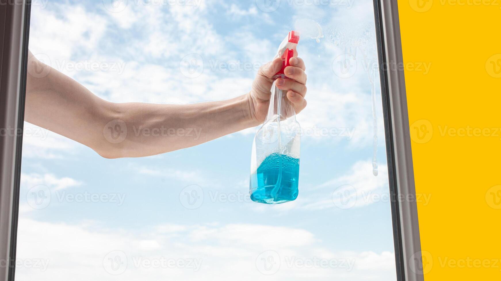 A man washes a window from the outside. The man sprays a blue cleaner photo