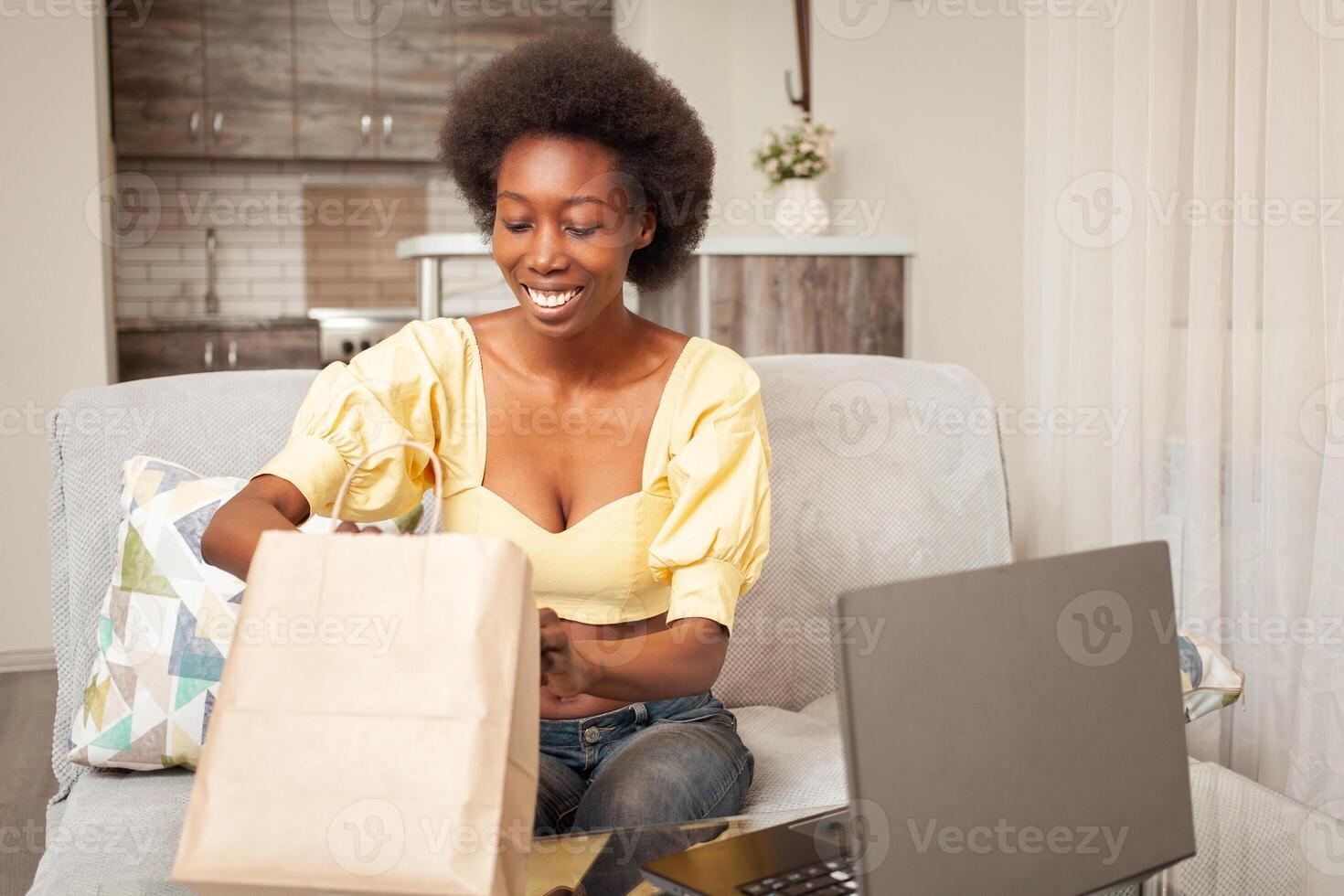 African American black woman at home sitting in front of laptop, online shopping, home delivery, bank card. Discounts promotions in the store. opens parcel photo