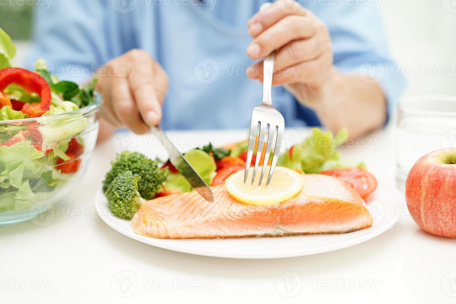 Asian elderly woman patient eating salmon stake and vegetable salad for healthy food in hospital. photo