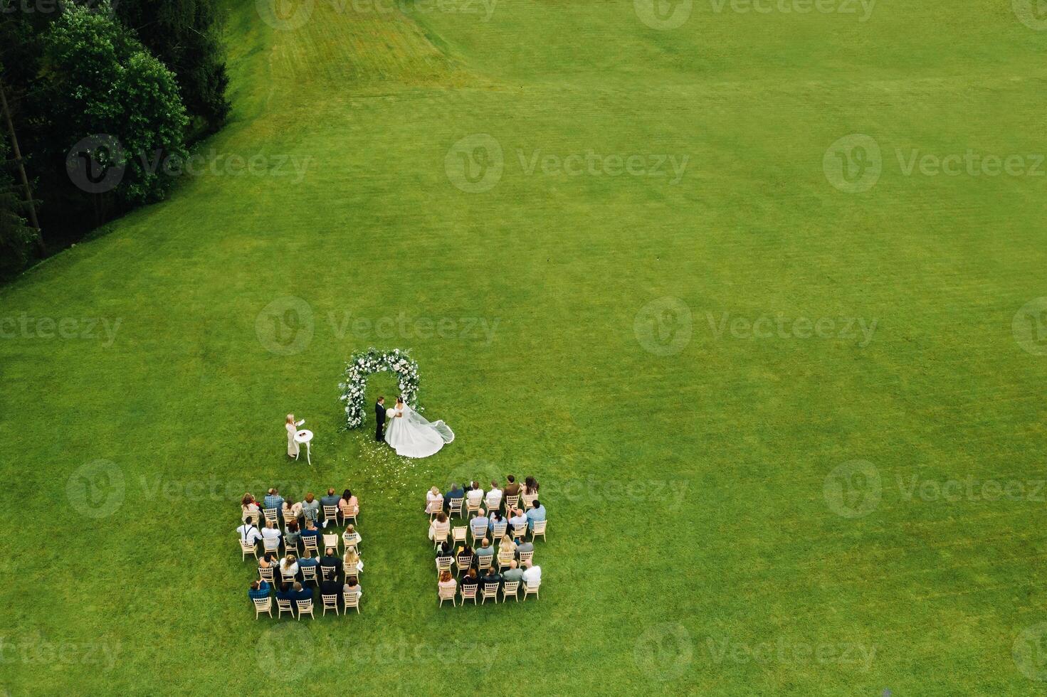 Top view of the Wedding ceremony in a green field with guests sitting on chairs. Wedding venue on the green lawn. photo
