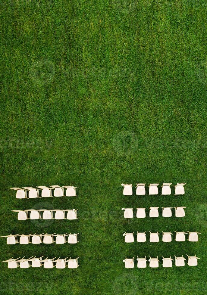 Top view of White wooden chairs standing in rows on a green field waiting for guests.View from a height of many white chairs standing on a green lawn photo