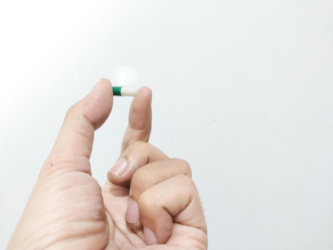 Fingers of a hand holding a capsule pill isolated on a white background photo