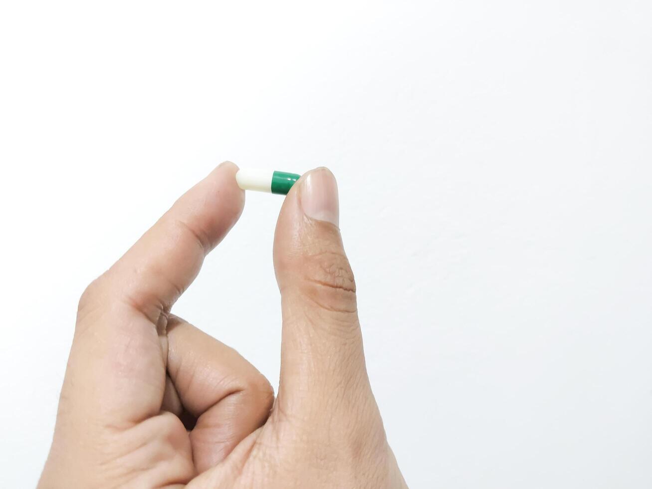 Fingers of a hand holding a capsule pill isolated on a white background photo